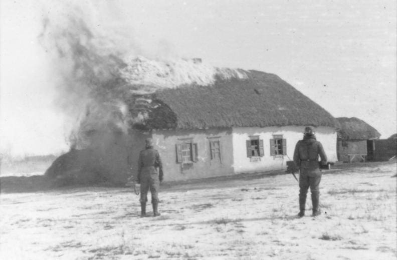 February 1943. Sowjetunion, Raum Charkow.- Zwei Soldaten der Waffen-SS vor einem brennende Gebäude (Bauernhaus) stehend; SS-PK Bild 101III-Zschaeckel-186-37